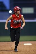 Softball girl player in equipment and uniform, running on the field, on the competition