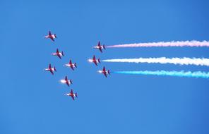 Flying red arrows, with white contrails, in the blue sky