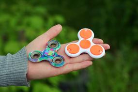 Colorful, patterned fidget spinners on the hand of the woman, at blurred background with the green plants