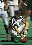 Football referee in black and white clothing holding the ball on the green field