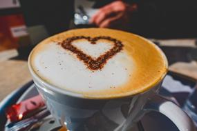 Beautiful cup of coffee, with the beautiful heart drawing on the brown and white foam