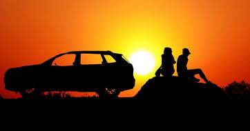 silhouettes of romantic couple near the car at sunset