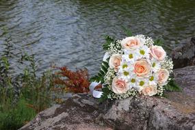 Beautiful wedding bouquet with white and orange roses, on the rocky shore