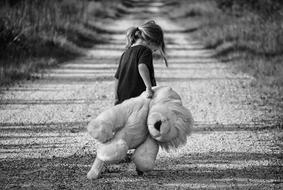 black and white photo girl drags a teddy lion along a country road