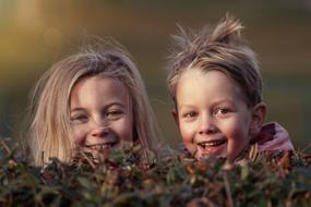 disheveled children peeping from behind a bush