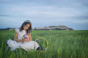 girl in a white dress with a bouquet of flowers is sitting in a meadow