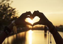 Hands in heart shape, on the beautiful shore, at colorful sunset, in the summer