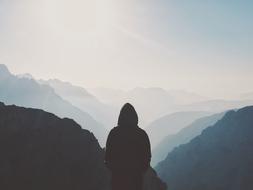 lonely man in a hood on top of a foggy mountain range