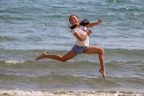 Smiling girl, jumping on the beautiful beach, near the water with waves