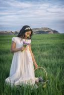 girl in a white dress with a basket of flowers in the meadow