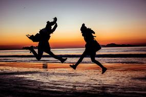 photo of two jumping people on the evening beach