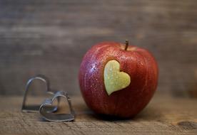 white heart on side of red apple and metal hearts at wooden surface
