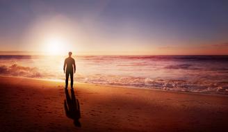 Silhouette of a man, on the beautiful, sandy beach, near the water with waves, at colorful sunset on horizon