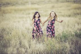 Sisters in the colorful dresses, walking on the beautiful, yellow and green field, with the plants
