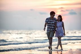 young Couple walks Holding Hands through water ar surfline