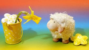 colorful Easter Background, cute toy Sheep looking at yellow flower