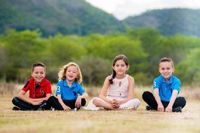 four happy kids sit on ground at forest with the mountains on background