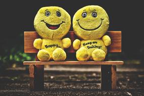 two Plush Yellow toy Smilies on bench