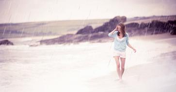 Girl, walking on the beautiful sandy beach, with the rocks, in the rain