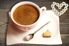 cup of coffee, spoon and biscuit on a saucer with flowers on the wooden table