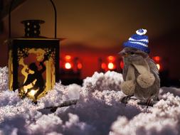 lantern and sparrow with a hat and a scarf in the snow