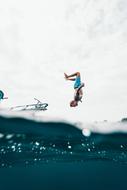 People jumping from the boat in into the beautiful blue water under cloudy sky