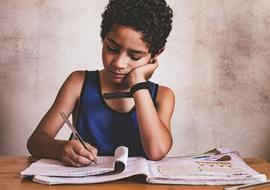 Child with the curly hair and wrist watch, writing in the notepad, with the pen