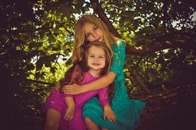 Young and child Girls sit together beneath tree, Sisters