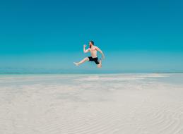 man is jumping on a tropical beach