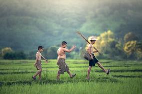 three asian boys walking through green field at scenic landscape