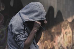 addict in the hoodie with syringe near the wall
