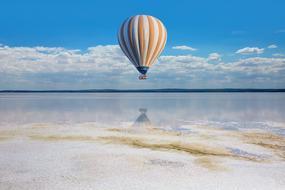 Colorful hot air balloon, flying above the water, near the sandy beach, under the blue sky, with clouds