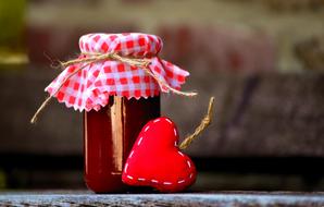 Beautiful still life with the glass jar with red jam, with red and white, checkered cloth with cord, and red heart