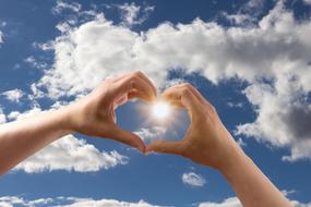 heart shape on hands against blue sky background