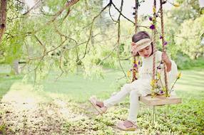 Cute girl on the swing, among the colorful plants, in sunlight, in the summer