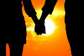 Silhouette of the lovers holding each others hand at background with the colorful sunset