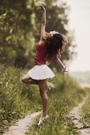 Dancing girl in red t-shirt and white shirt, on the beautiful path in green plants