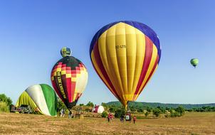 People, around the colorful, patterned hot air balloons, above the beautiful and colorful mountains