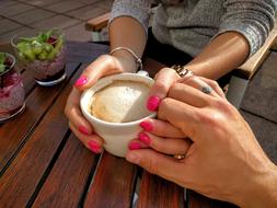 hands of lovers hold a cup of cappuccino