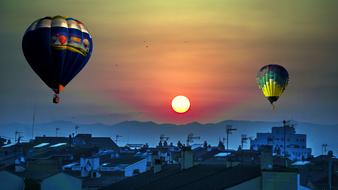 Beautiful, flying, colorful hot air balloons, above the city near the mountains, at colorful dawn on background