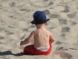 boy in a blue hat plays with sand on the beach