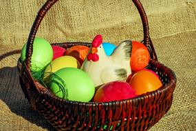 figurine of a rooster and multi-colored eggs in a wicker basket