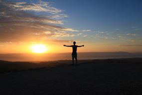 man stands with wide open hands at sunrise sky