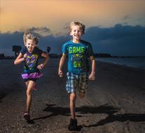 Smiling children, running on the beautiful sandy beach, at colorful, cloudy sky