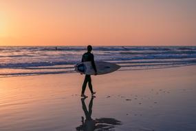 surfer with a board on the beach against the background of a beautiful sunset, san diego, california