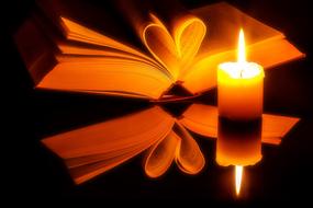 open bible and burning candle in the dark