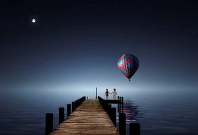 Fantastic image of a couple in love on the pier and hot air balloon against the night sky