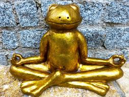 Beautiful, shiny, golden statue of the frog in meditation, near the stone wall