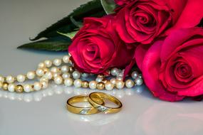 a bouquet of red roses, pearl beads and wedding rings