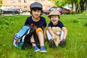 two happy Boys in caps sitting on lawn